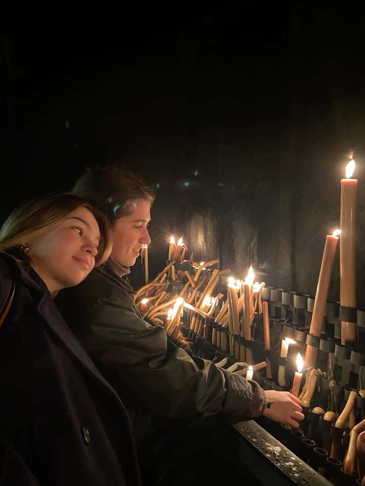 A couple lighting candles side by side in a darkened church