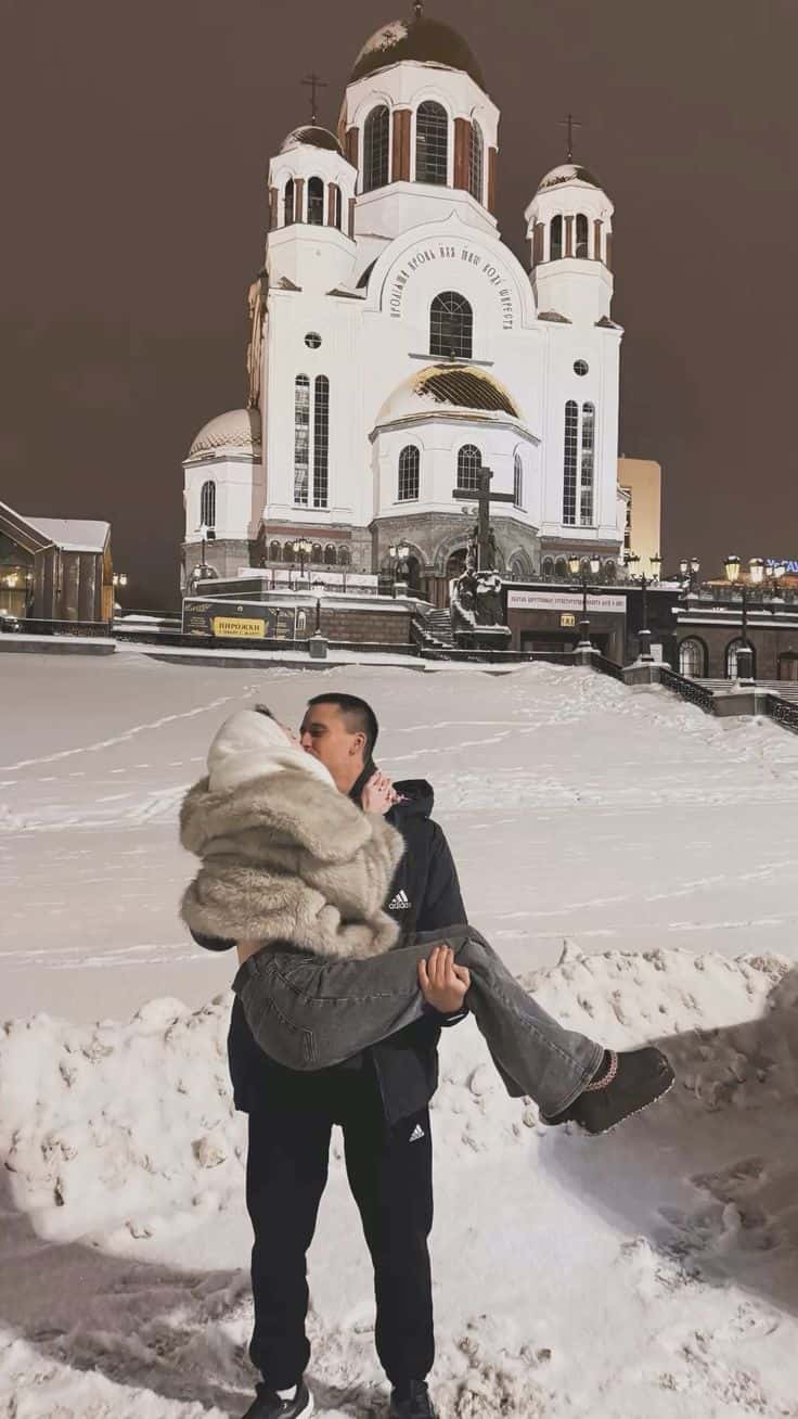 A couple in the snow outside a floodlit cathedral