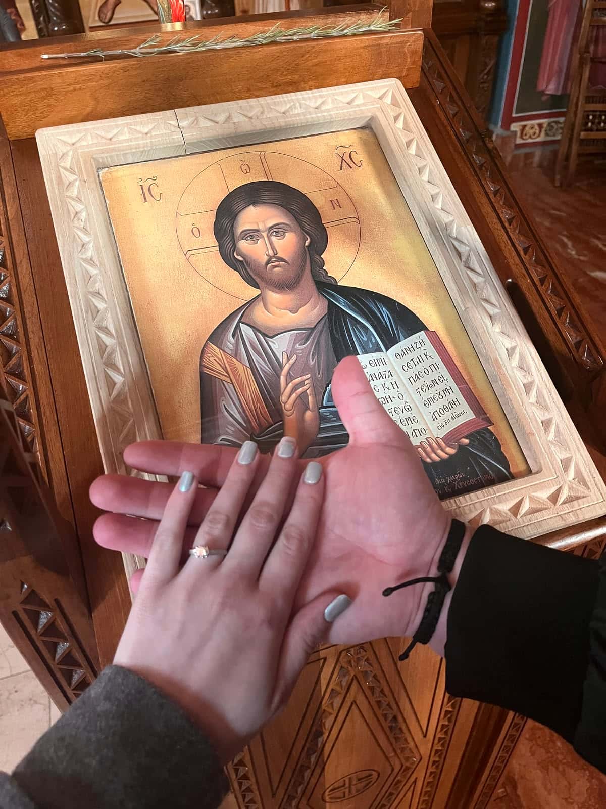 A newly engaged couple holding hands before an icon of Christ