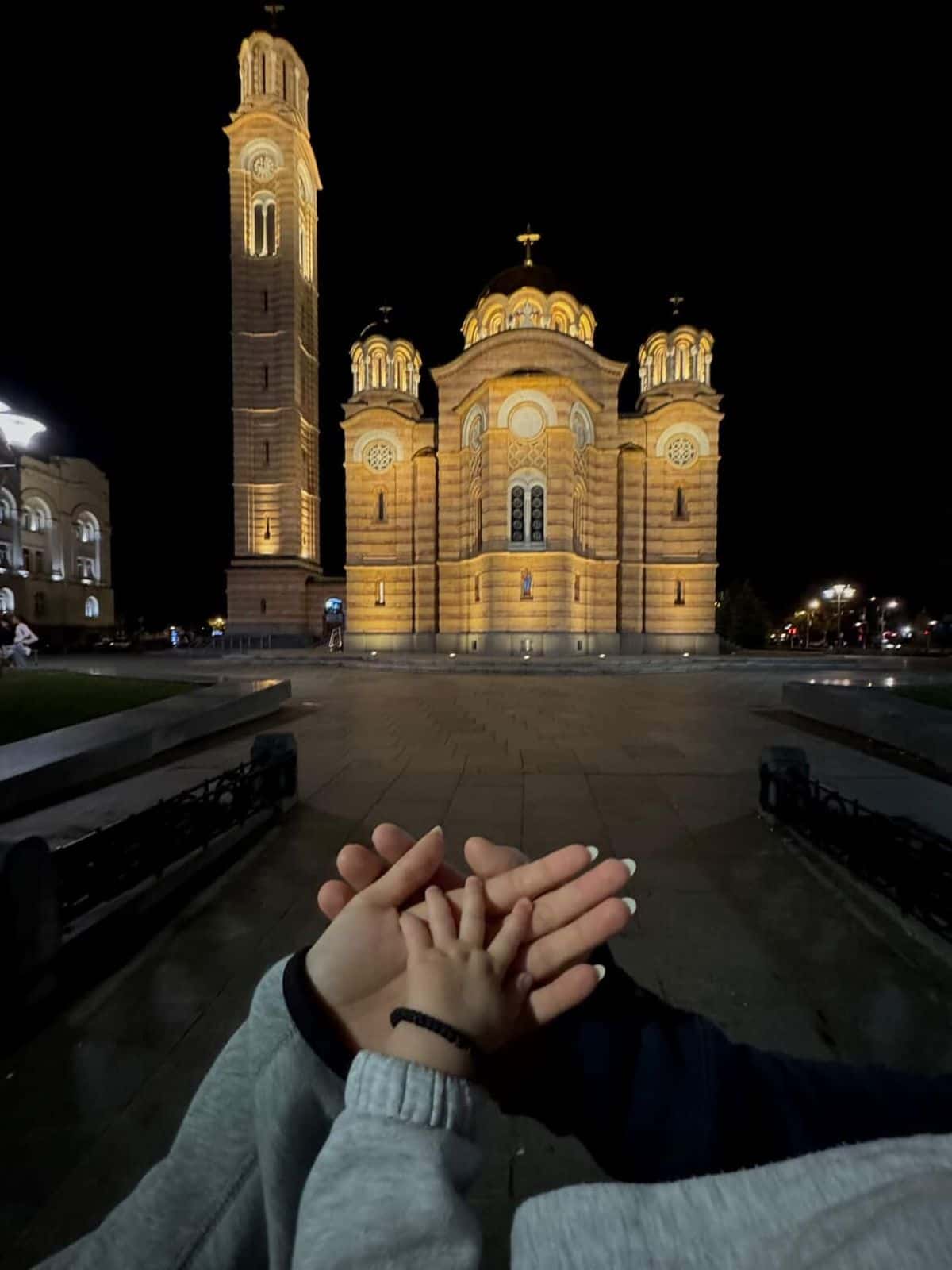 Two hands resting together in front of a cathedral at night